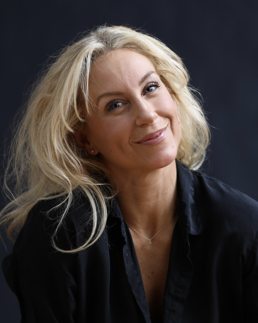 Platinum blonde middle aged woman wearing black shirt and smiling against black background