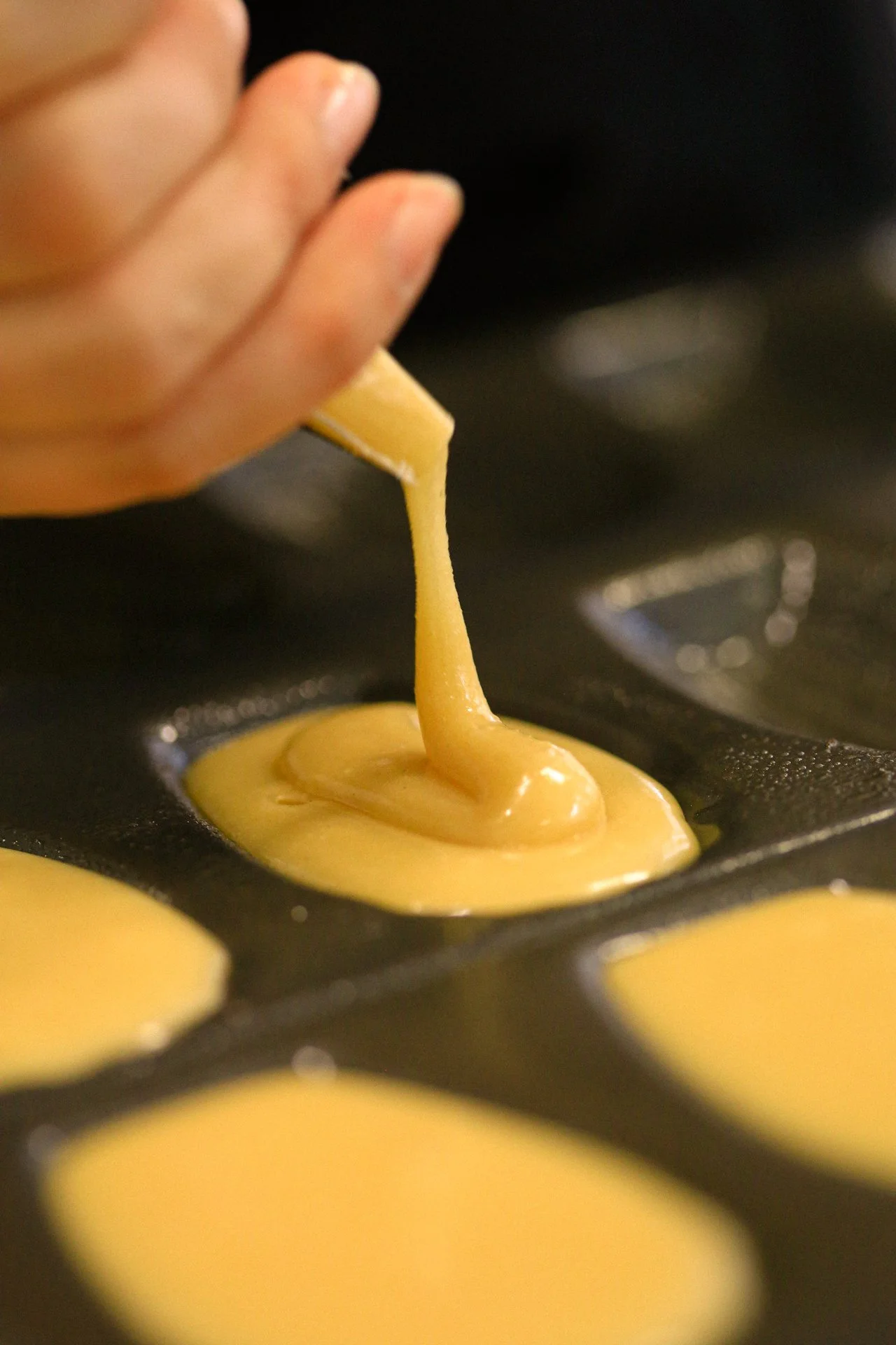 Pouring yellow batter into a mini muffin tin for baking.