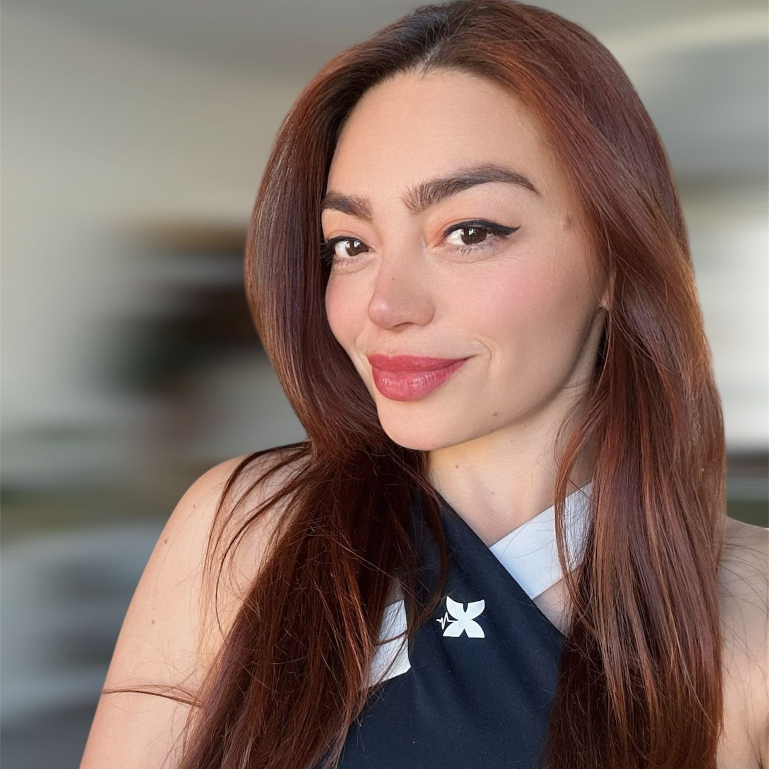 Close-up of a woman with long red hair winking and smiling, wearing a navy and white uniform with a small white flower emblem.