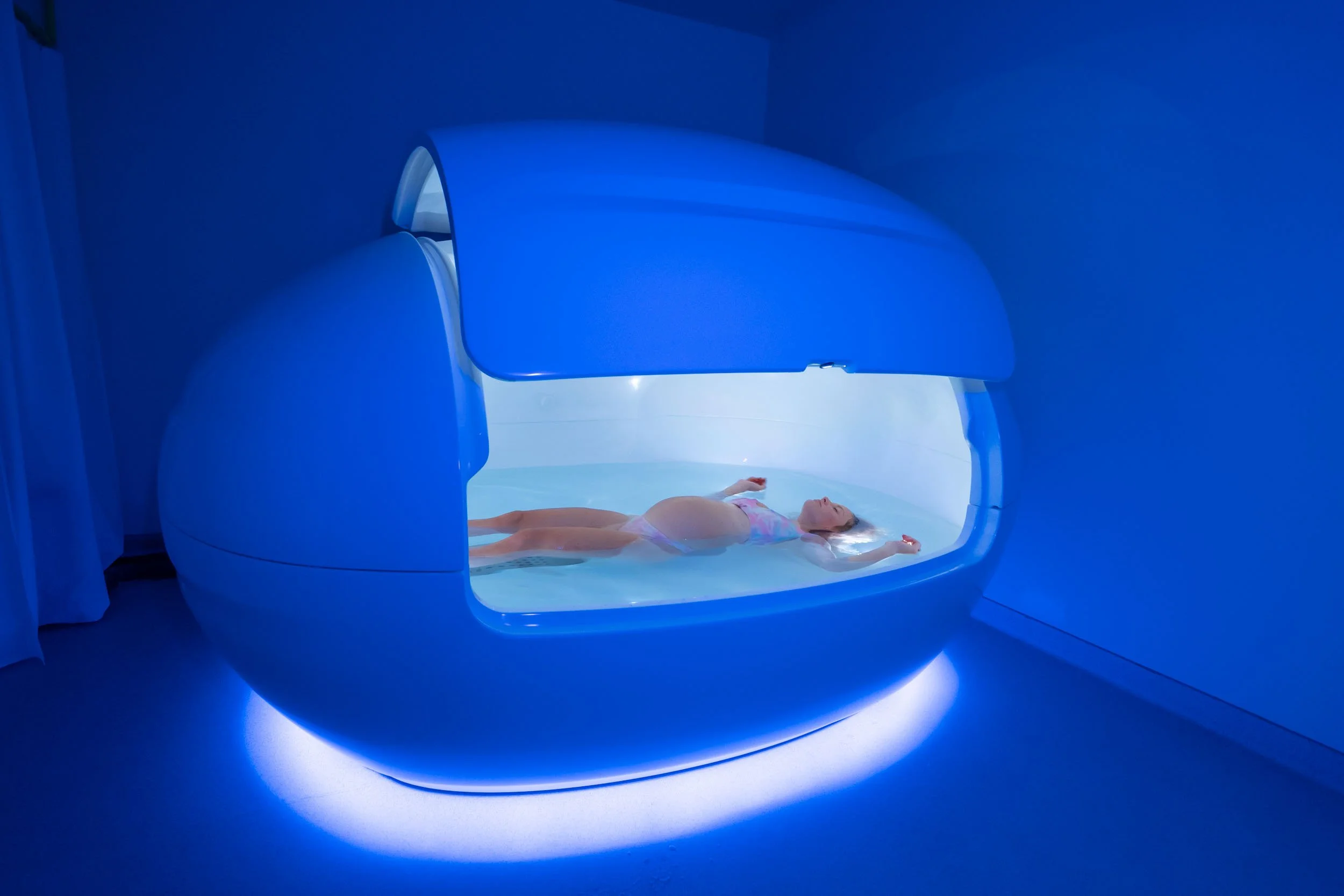 A woman lying inside an MRI machine, with the machine's door open, in a darkened room illuminated by blue light.