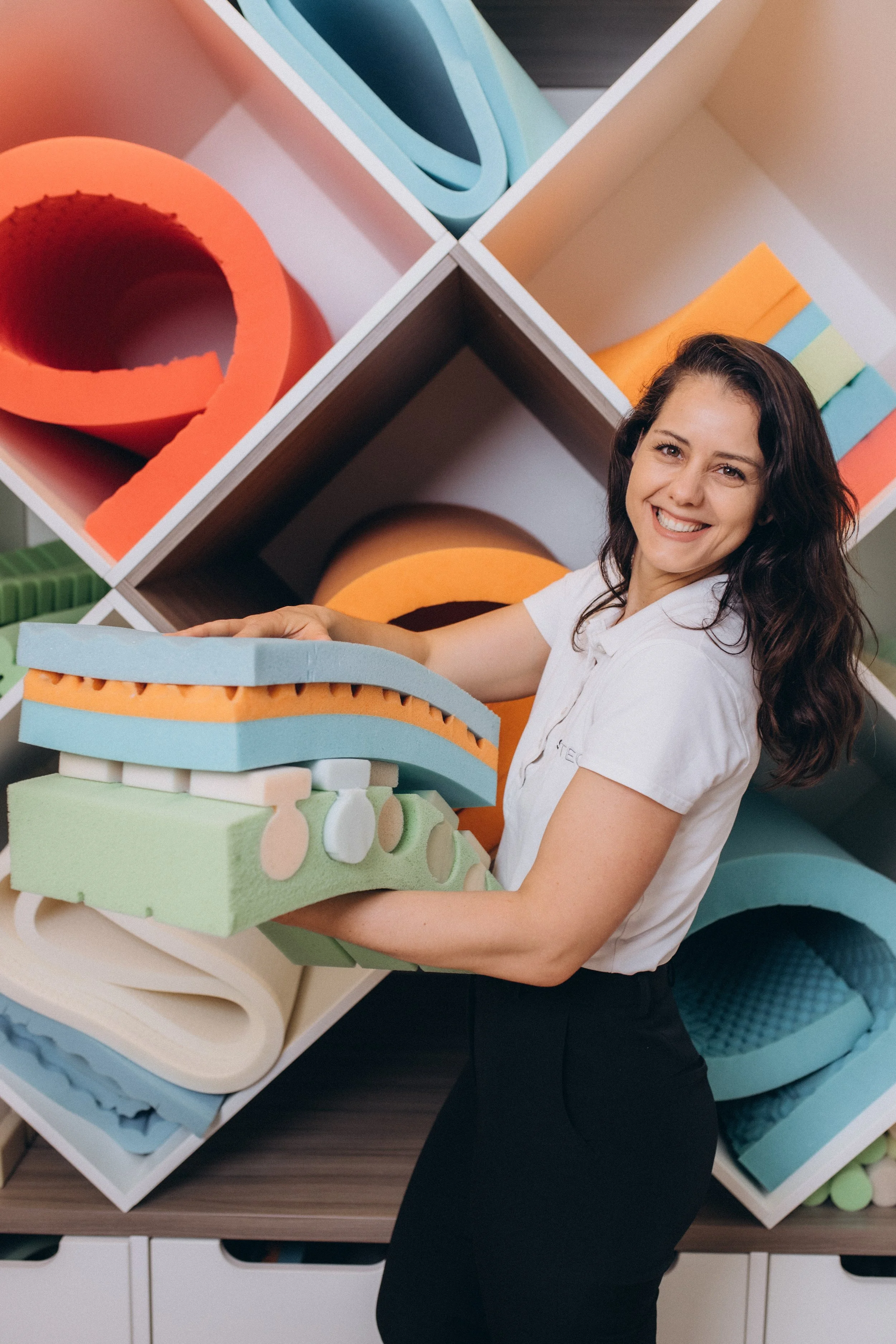 A woman holding colorful foam pieces in front of a display of foam shapes and crafting materials.