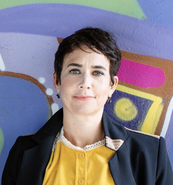 Middle aged smiling woman with brown pixie cut wearing yellow top and black blazer