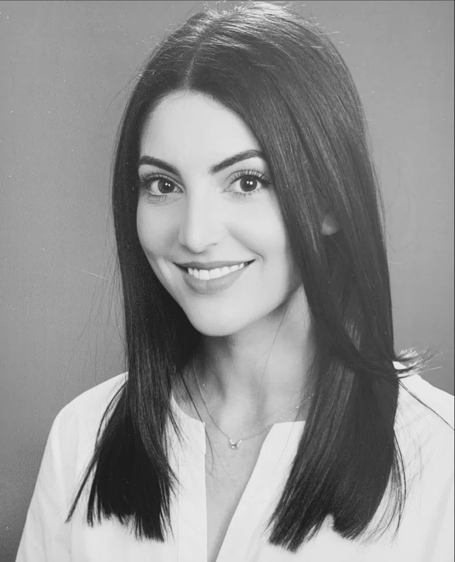 Black and white portrait of a smiling woman with straight, shoulder-length dark hair, wearing a white shirt and a delicate necklace.