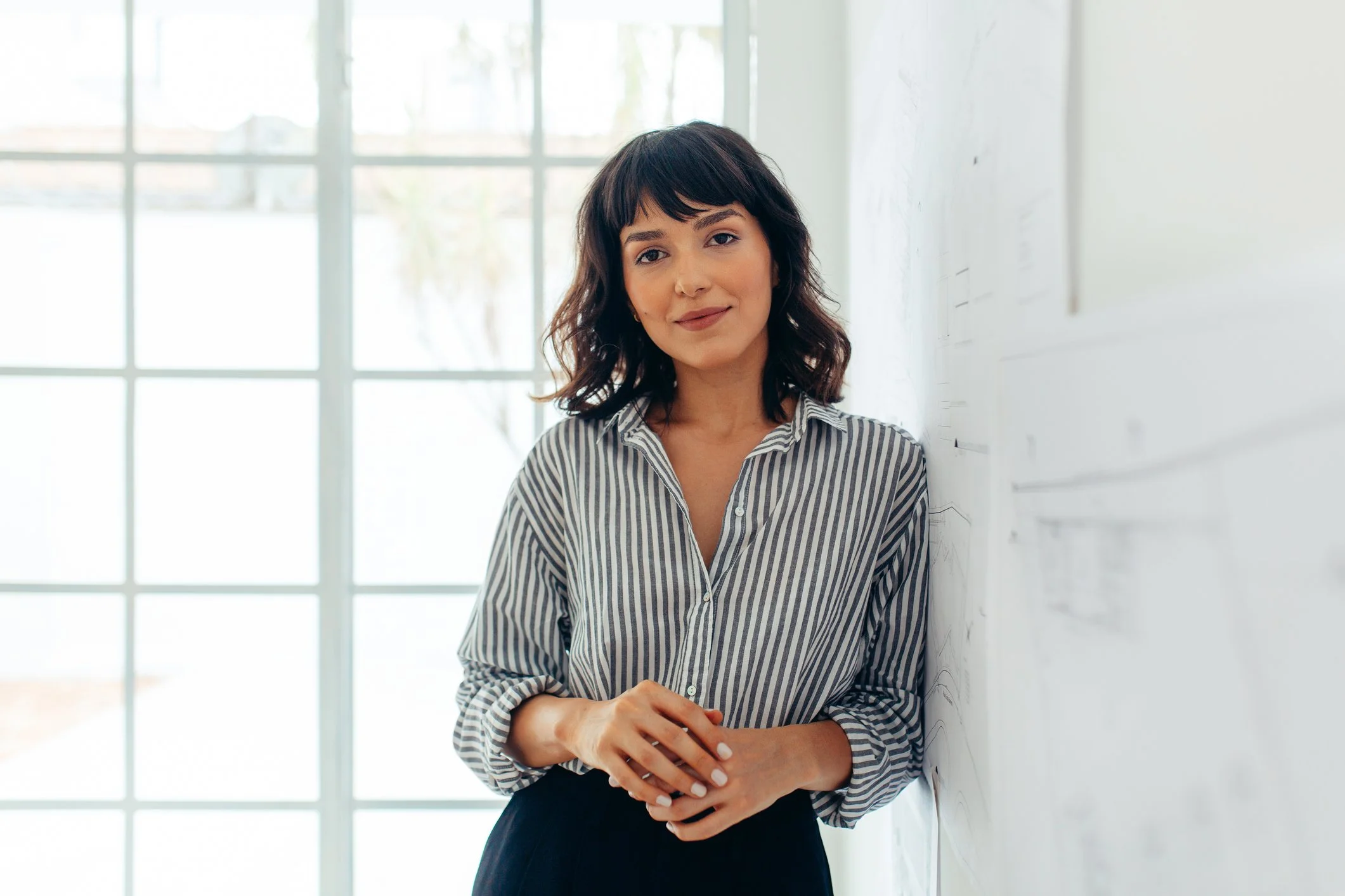 young brunette professional woman leaning against wall smiling thoughtfully