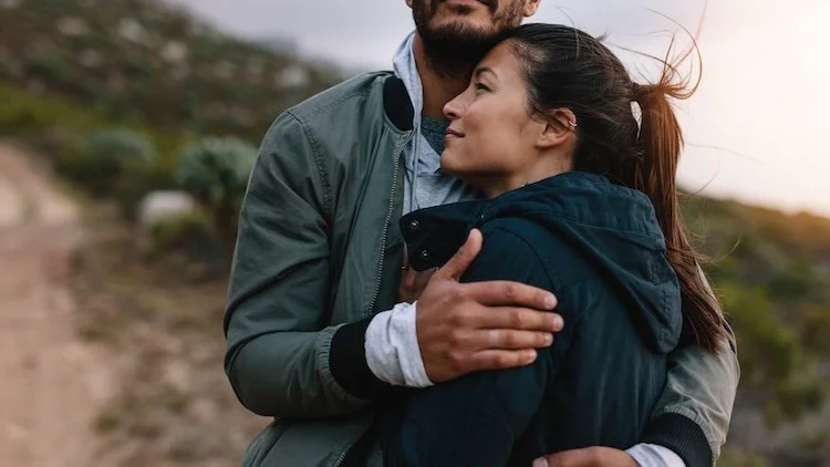young couple hugging outdoors with hopeful smile