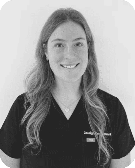 Caleigh Cruikshank, Nurse Practitioner with long wavy hair smiling, wearing a black shirt with a name tag, standing against a plain light-colored background at Hannam Fertility Centre Toronto