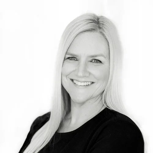 Black and white portrait of a smiling woman with long blonde hair wearing a dark top.