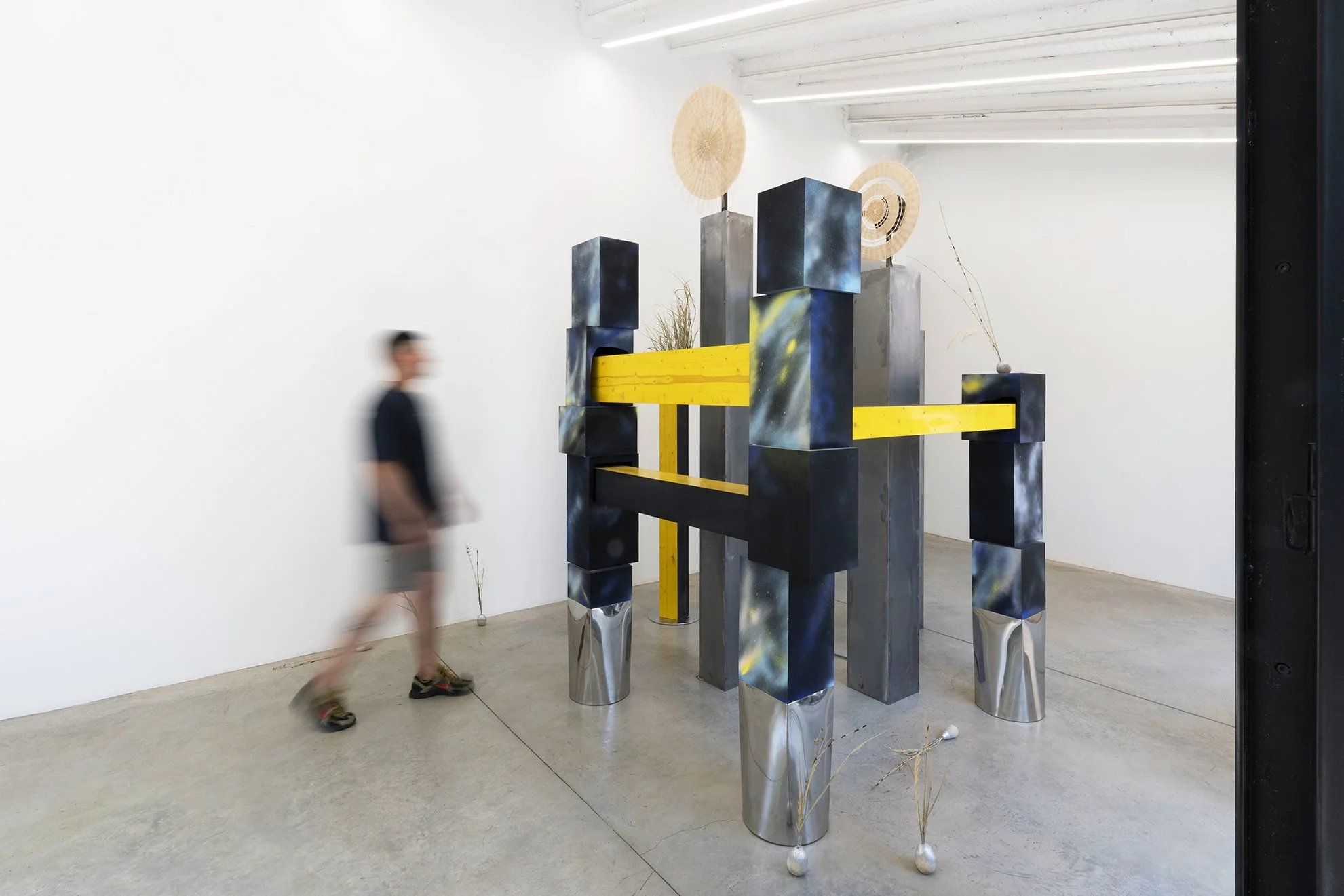 Leah Dixon. TARTAN TARTANA: The Girl Who Invented The Wheel IV, 2026. 
Site specific sculpture (indoor). Wood, steel, paint, enamel, woven basket wheels, rotary motors, molded sawdust and resin clay onions, natural rattan, esparto grass, horsetail re