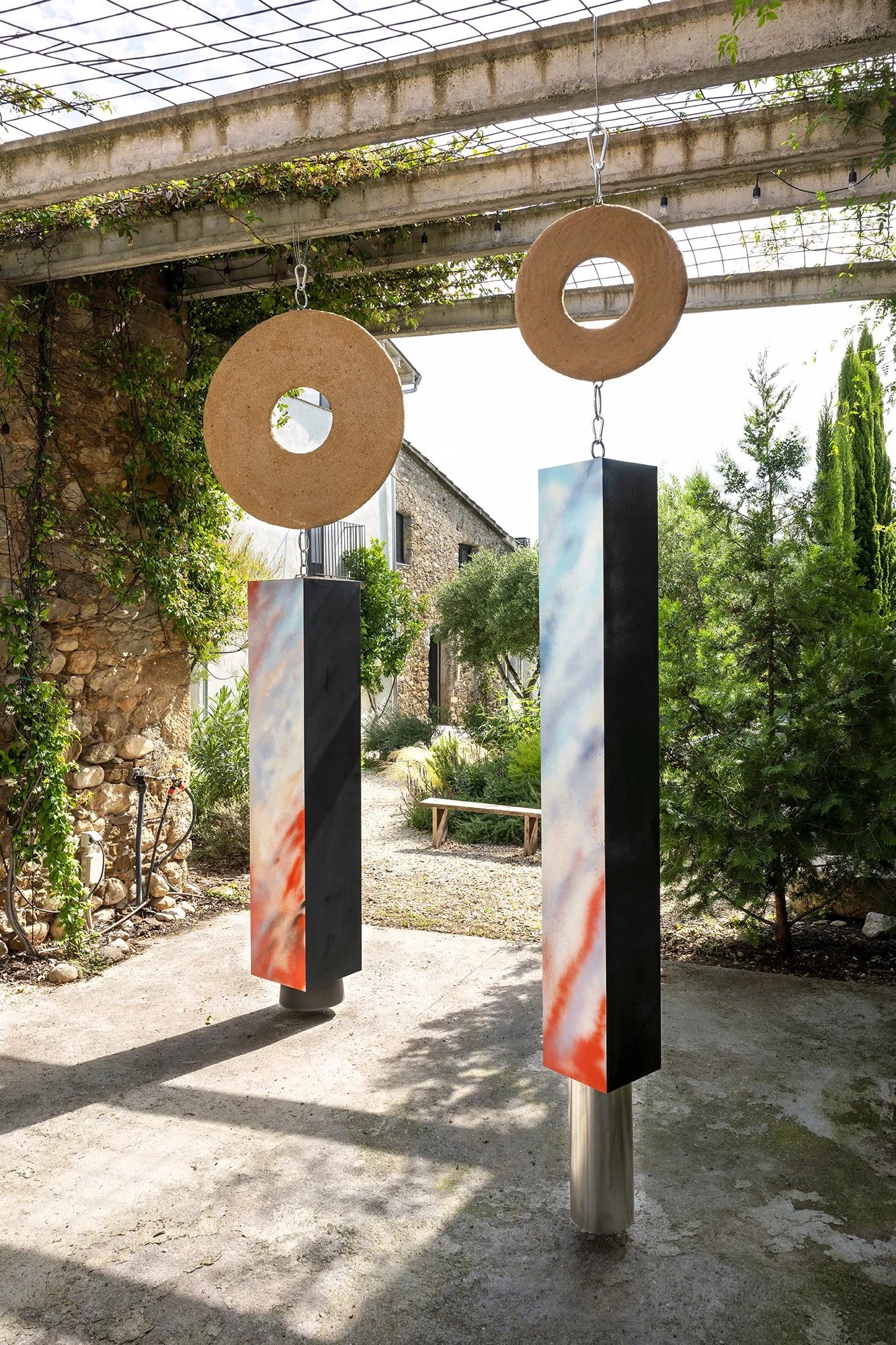 Leah Dixon. Megalithic Fireworks Portals, 2026.
Site specific sculpture (outdoor). Wood, paint, enamel, hand-pressed sawdust and resin clay discs, suspended aluminum pipe, suspended plastic bucket, metal hardware. 
230 x 150 x 375 cm. 