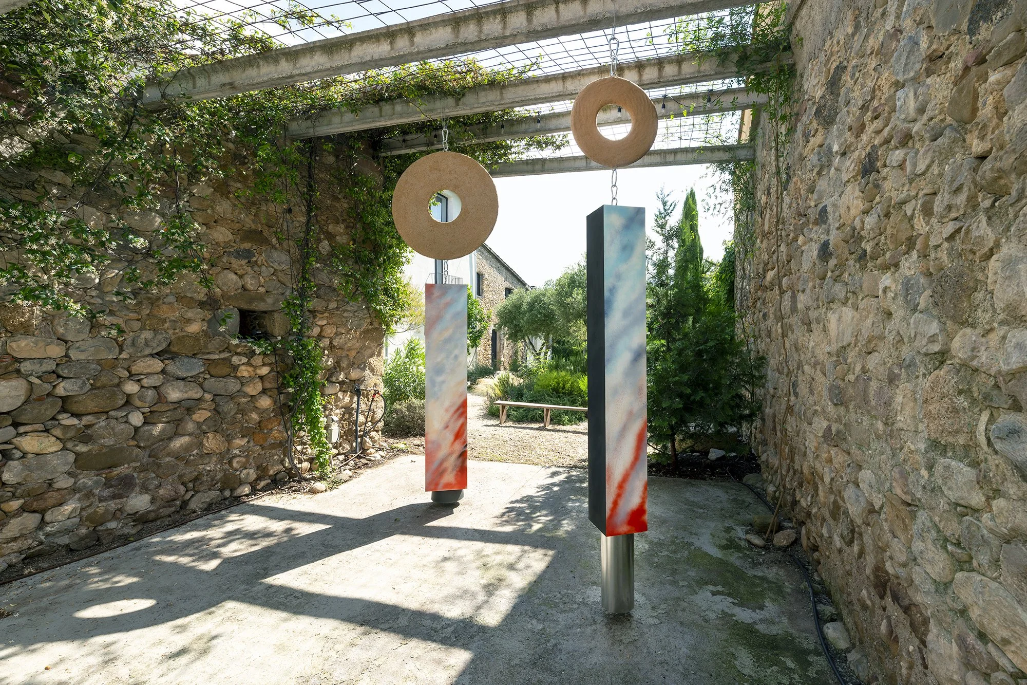 Leah Dixon. Megalithic Fireworks Portals, 2026.
Site specific sculpture (outdoor). Wood, paint, enamel, hand-pressed sawdust and resin clay discs, suspended aluminum pipe, suspended plastic bucket, metal hardware. 
230 x 150 x 375 cm. 