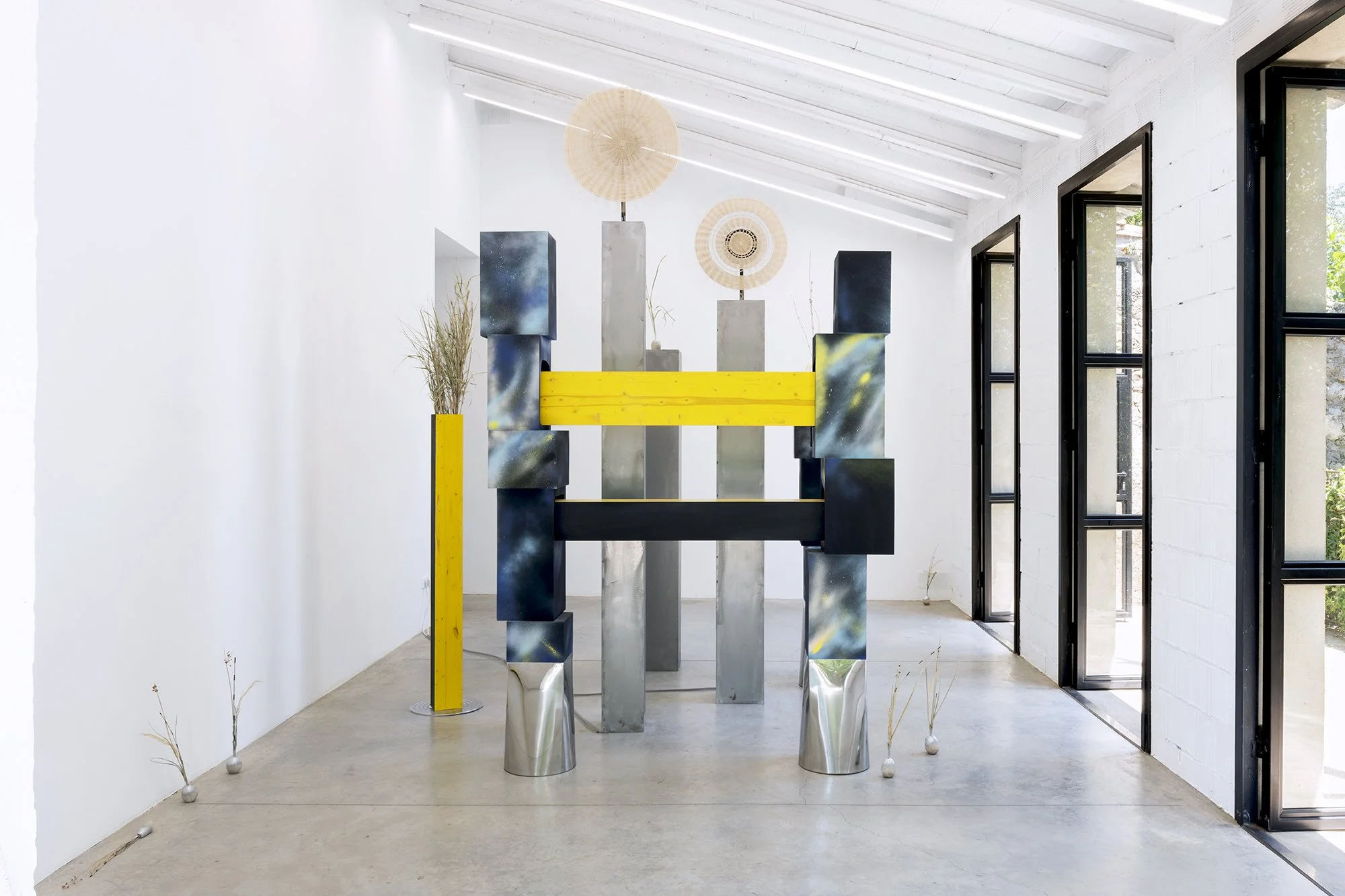 Leah Dixon. TARTAN TARTANA: The Girl Who Invented The Wheel IV, 2026. 
Site specific sculpture (indoor). Wood, steel, paint, enamel, woven basket wheels, rotary motors, molded sawdust and resin clay onions, natural rattan, esparto grass, horsetail re