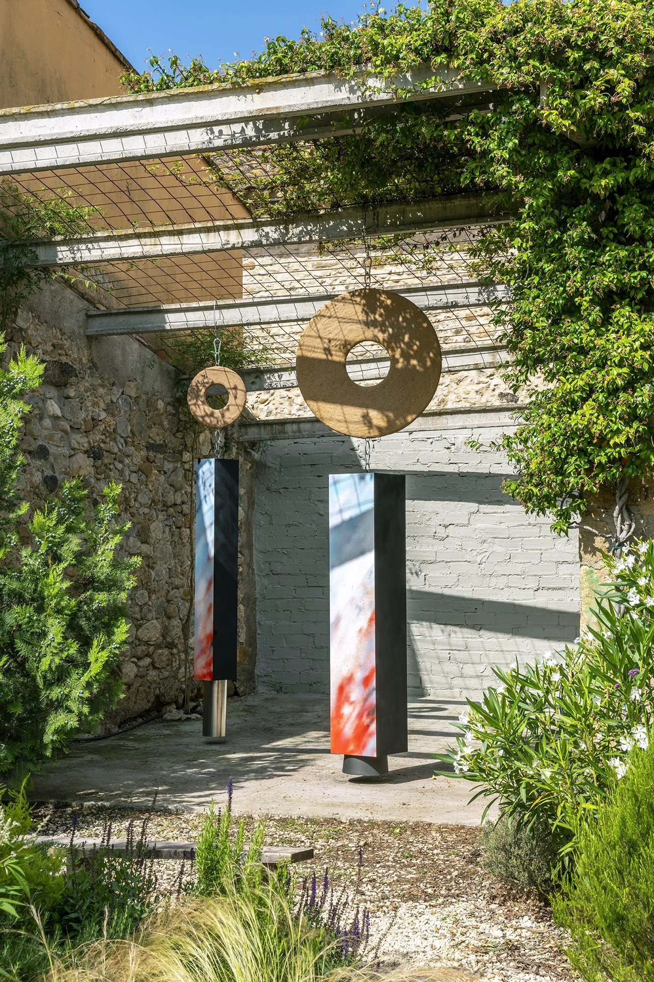 Leah Dixon. Megalithic Fireworks Portals, 2026.
Site specific sculpture (outdoor). Wood, paint, enamel, hand-pressed sawdust and resin clay discs, suspended aluminum pipe, suspended plastic bucket, metal hardware. 
230 x 150 x 375 cm. 