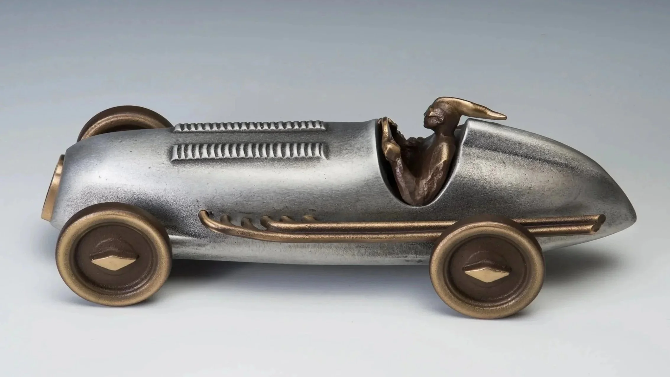 A toy race car made of metal with gold and bronze accents, featuring an imaginative creature with horns as the driver.