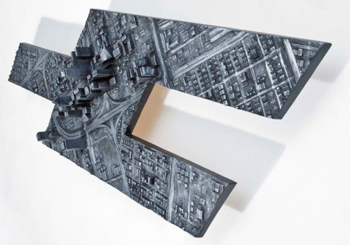 A modern art sculpture resembling a city map with detailed roads and buildings, mounted on a white base.