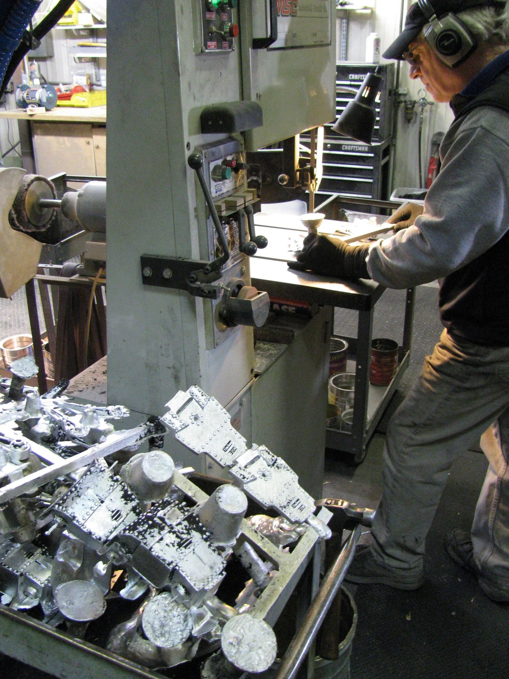 A person wearing safety goggles and gloves working on a metal casting mold at a workspace with tools and equipment.