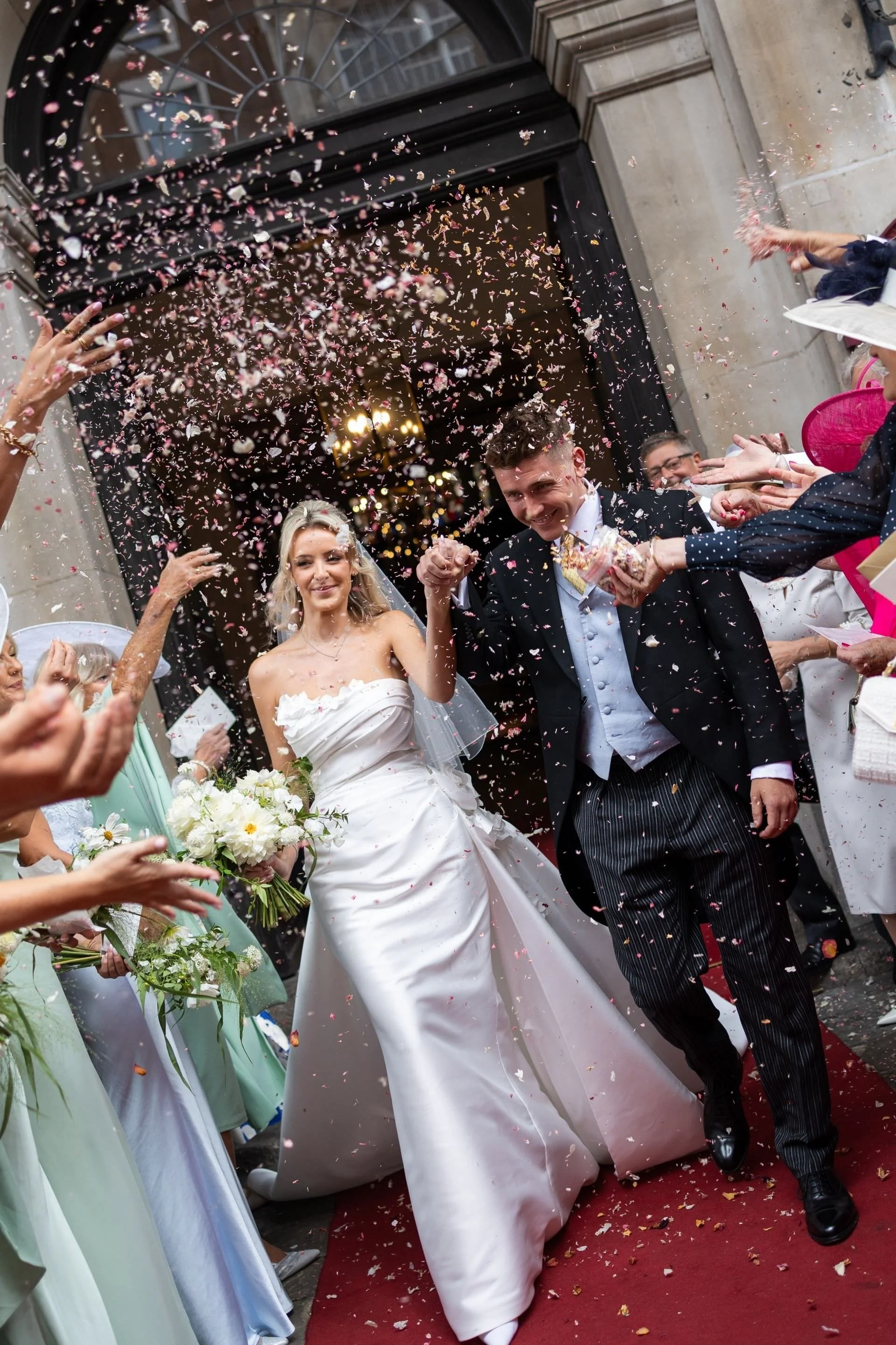 Bride and groom leaving their London wedding ceremony through falling confetti.