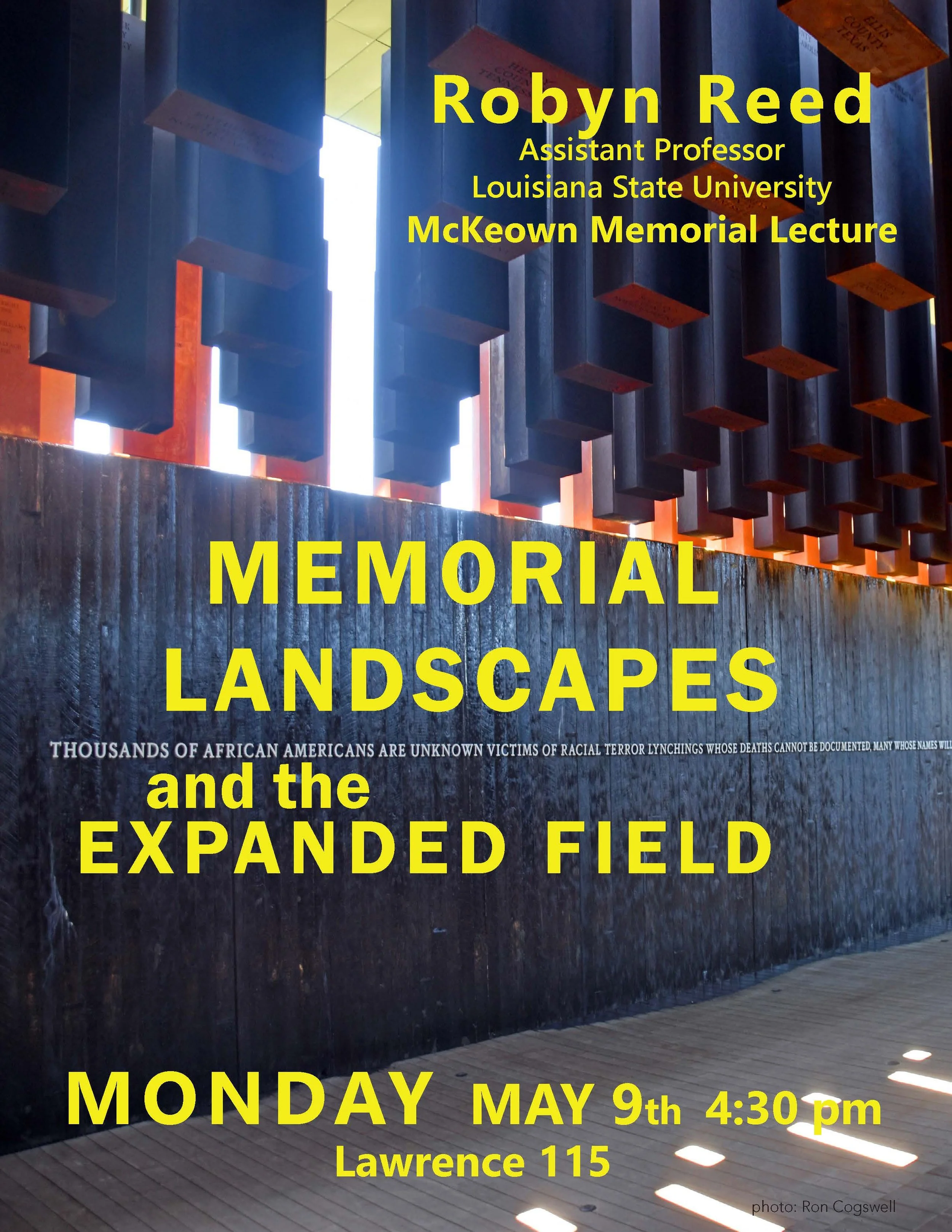A memorial exhibit with hanging metal plaques and large yellow text giving event details, including name of speaker, university, date, time, and location.