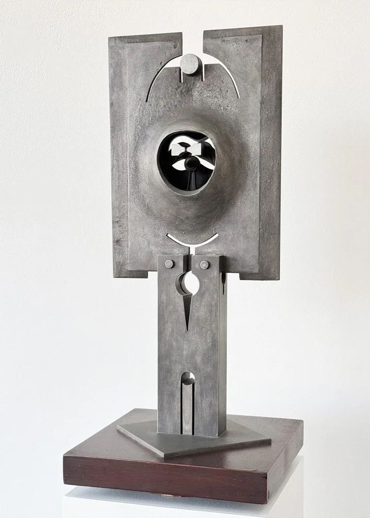 Abstract metal sculpture by Angelo Granata on a wooden base, featuring geometric shapes and a circular opening in the center.