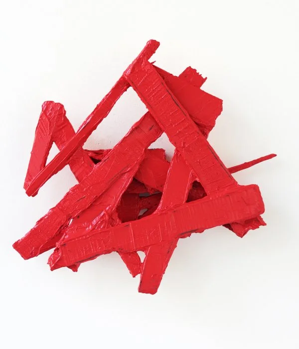 Abstract sculpture of red wooden planks arranged in a chaotic, intersecting pattern on a white background. Artwork by Felix Becker.