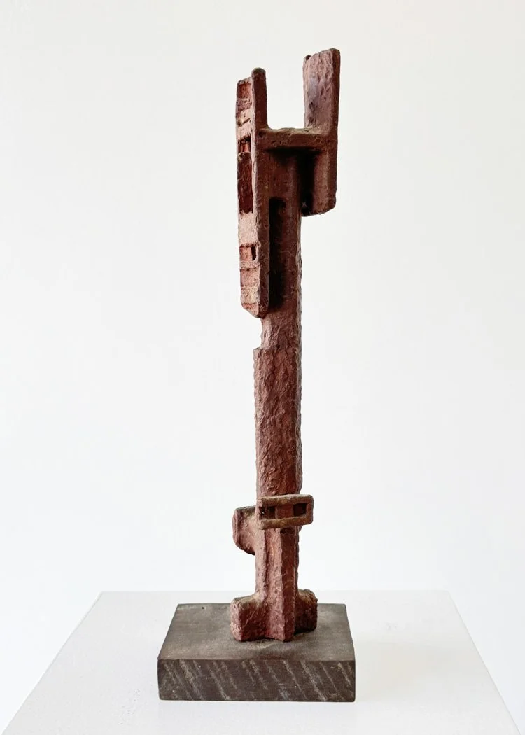 Abstract clay sculpture by Angelo Granata on a wooden base, with vertical and horizontal elements, resembling a stylized figure.