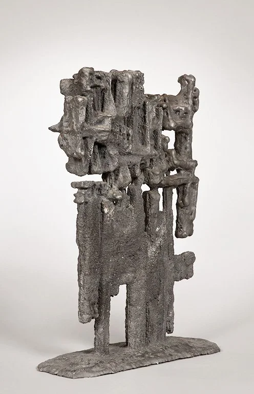 Abstract metal sculpture titled HETEROS by Angelo Granata in gray tones, featuring irregular and jagged forms with a vertical orientation and textured surface.