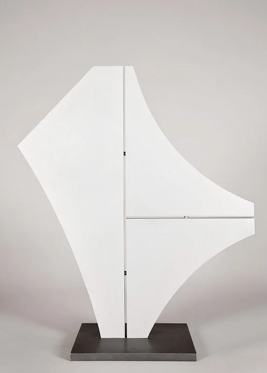 Abstract geometric aluminum sculpture by Angelo Granata on a dark base, featuring angular and curved shapes, against a neutral background.