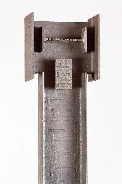 Close-up of a modern minimalist iron sculpture by Angelo Granata resembling a capital "I" with intricate patterns.