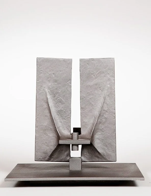 Abstract metal sculpture by Angelo Granata with two vertical slabs and central support on a flat base against a neutral background.