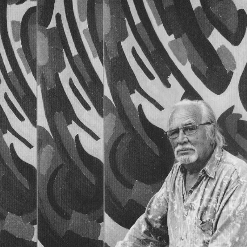 Belgian artist Léopold Plomteux with glasses in front of a large patterned mural, featuring bold abstract designs and shapes, in black and white.