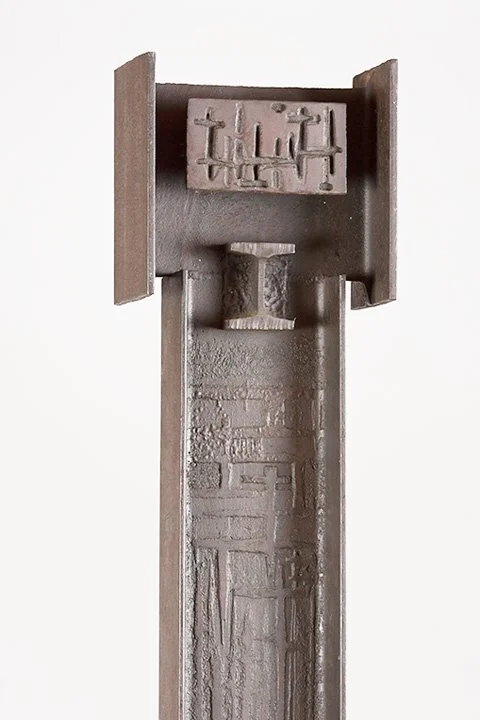 Abstract metal sculpture by Angelo Granata with geometric shapes and textured surface, featuring a vertical column and a small horizontal block at the top.