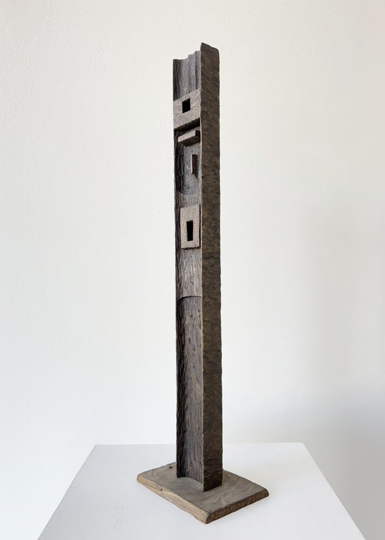 Tall wooden sculpture by Angelo Granata with geometric cutouts on a simple base, minimalist design against a plain background.