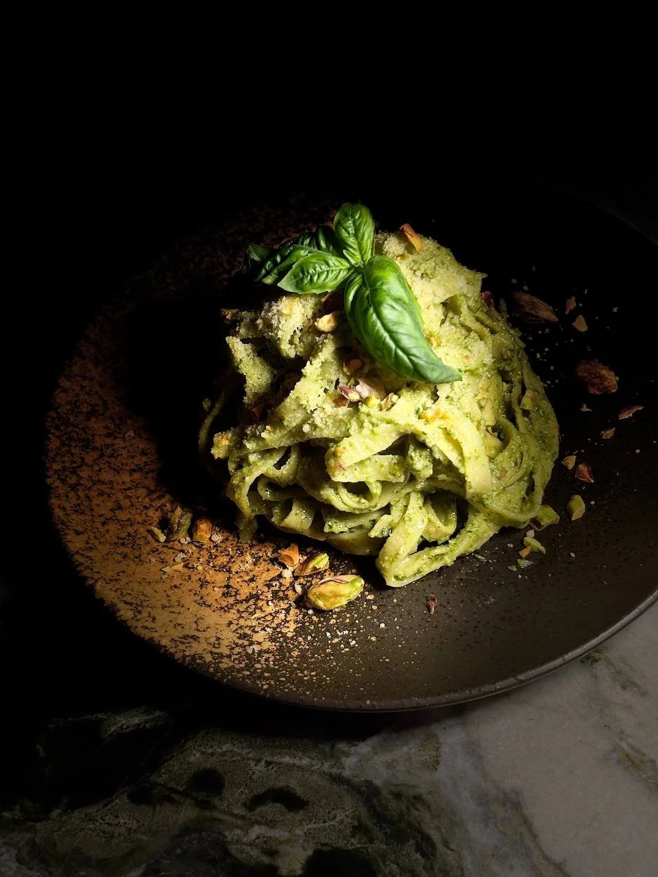 Plate of green pasta garnished with fresh basil leaves and crushed pistachios.