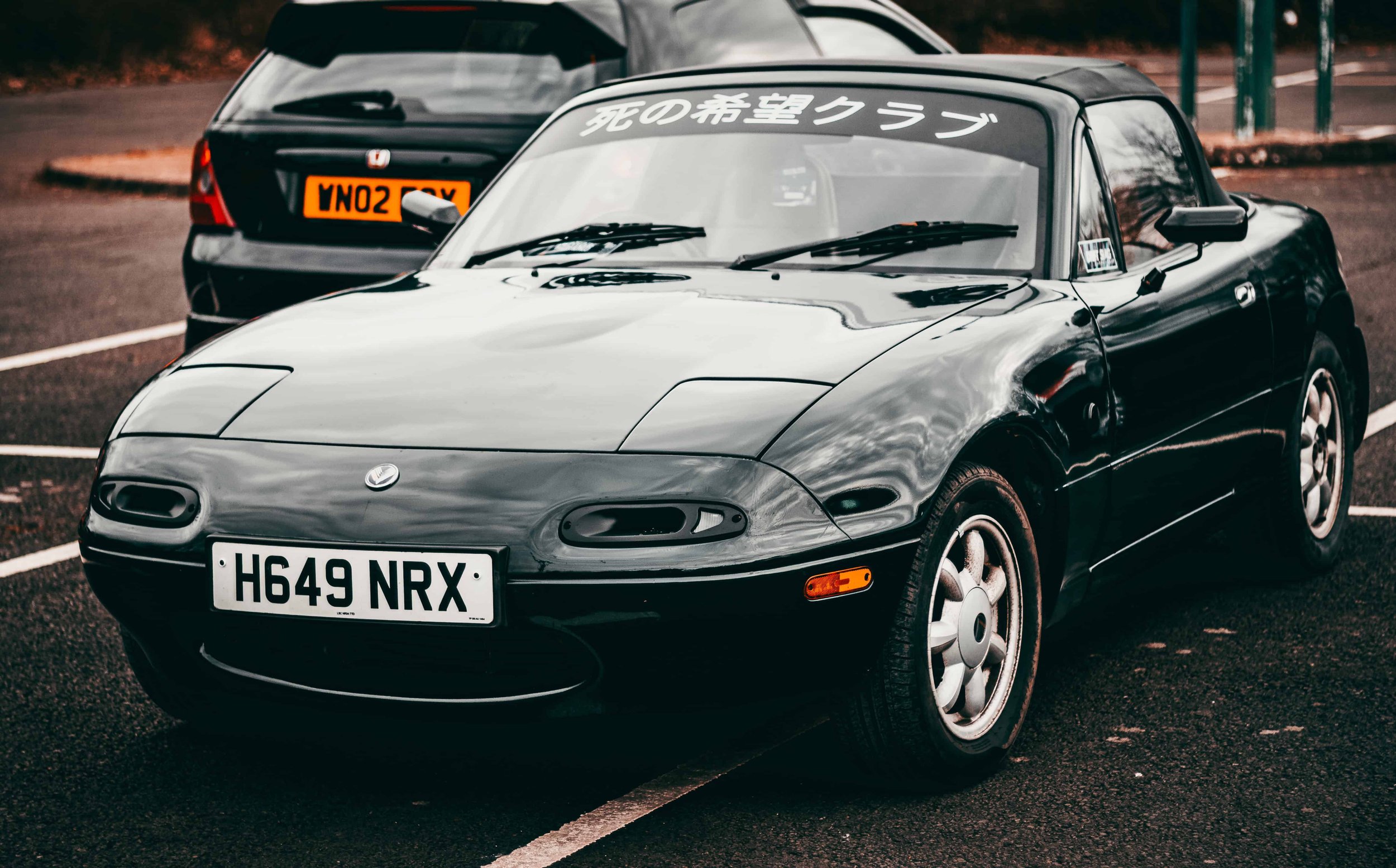 Black sports car parked with a visible license plate "H649 NRX" in a parking lot.