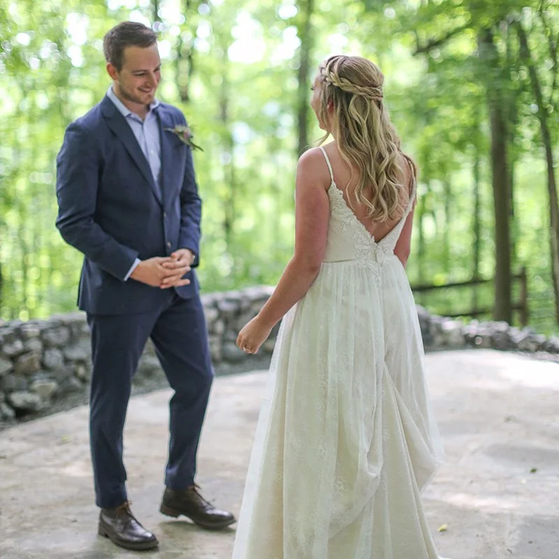 A couple exchanging vows outdoors in a wooded area, with the woman in a white wedding dress and the man in a blue suit.