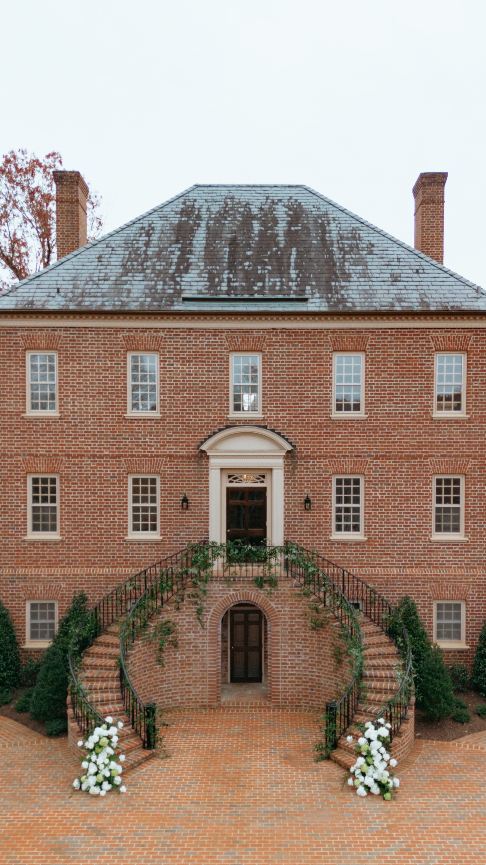 A red brick mansion with a curved brick staircase, white floral decorations, and multiple windows.