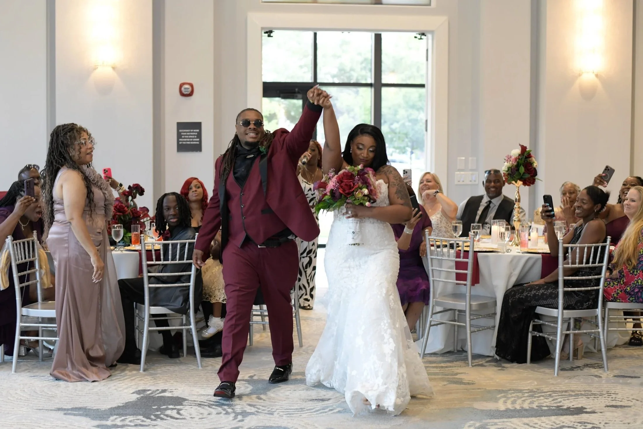 A bride and groom dance together at a wedding reception while guests watch and take photos.