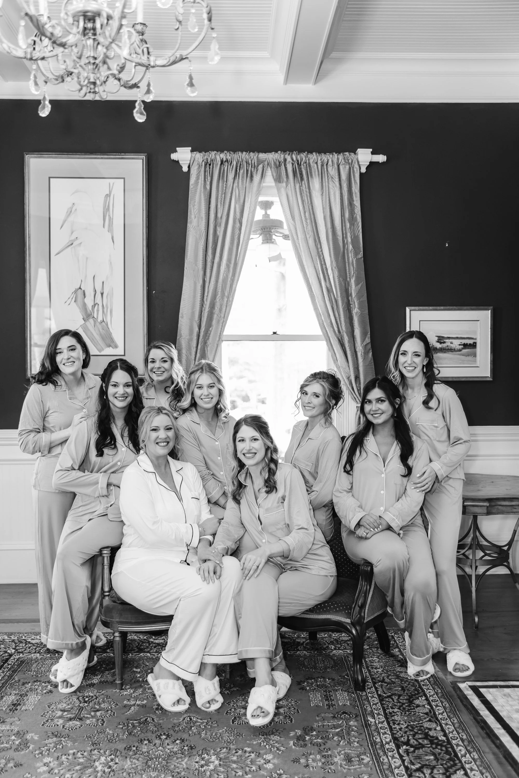 A group of nine women in pajamas sitting and standing in a living room, smiling for a photo.