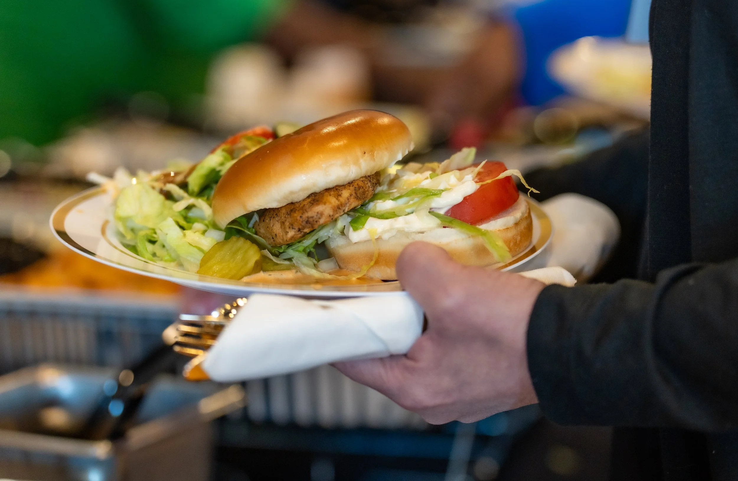 Hand holding a plate with a sandwich and salad at a buffet.