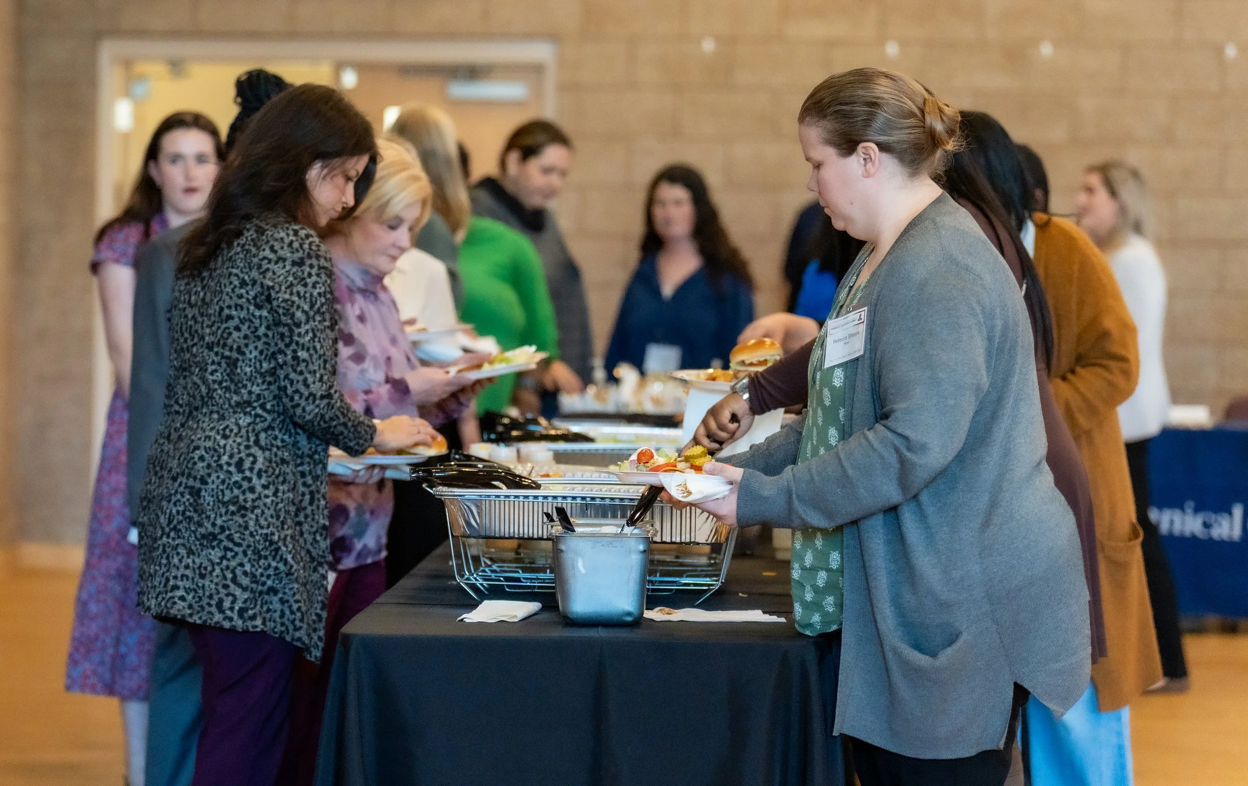 People lined up at a buffet table selecting food at a gathering or conference.