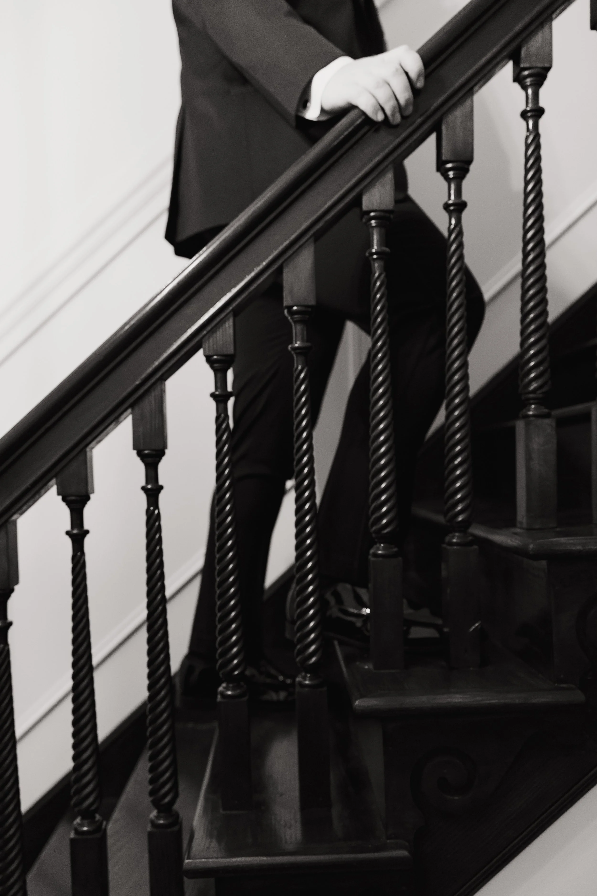Person in a suit holding onto a staircase handrail with black balusters.