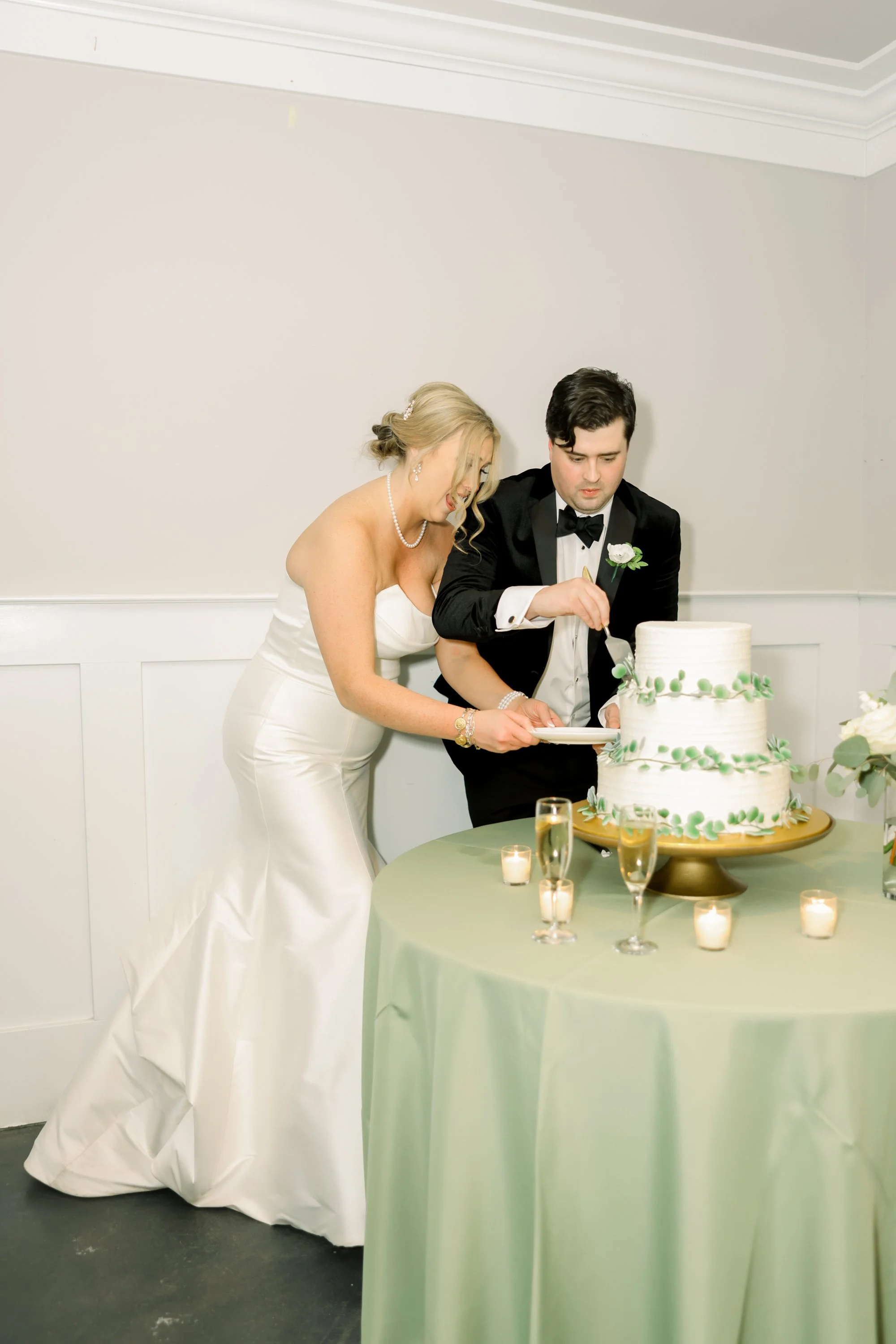 Bride and groom cutting wedding cake with candles and champagne glasses on the table.