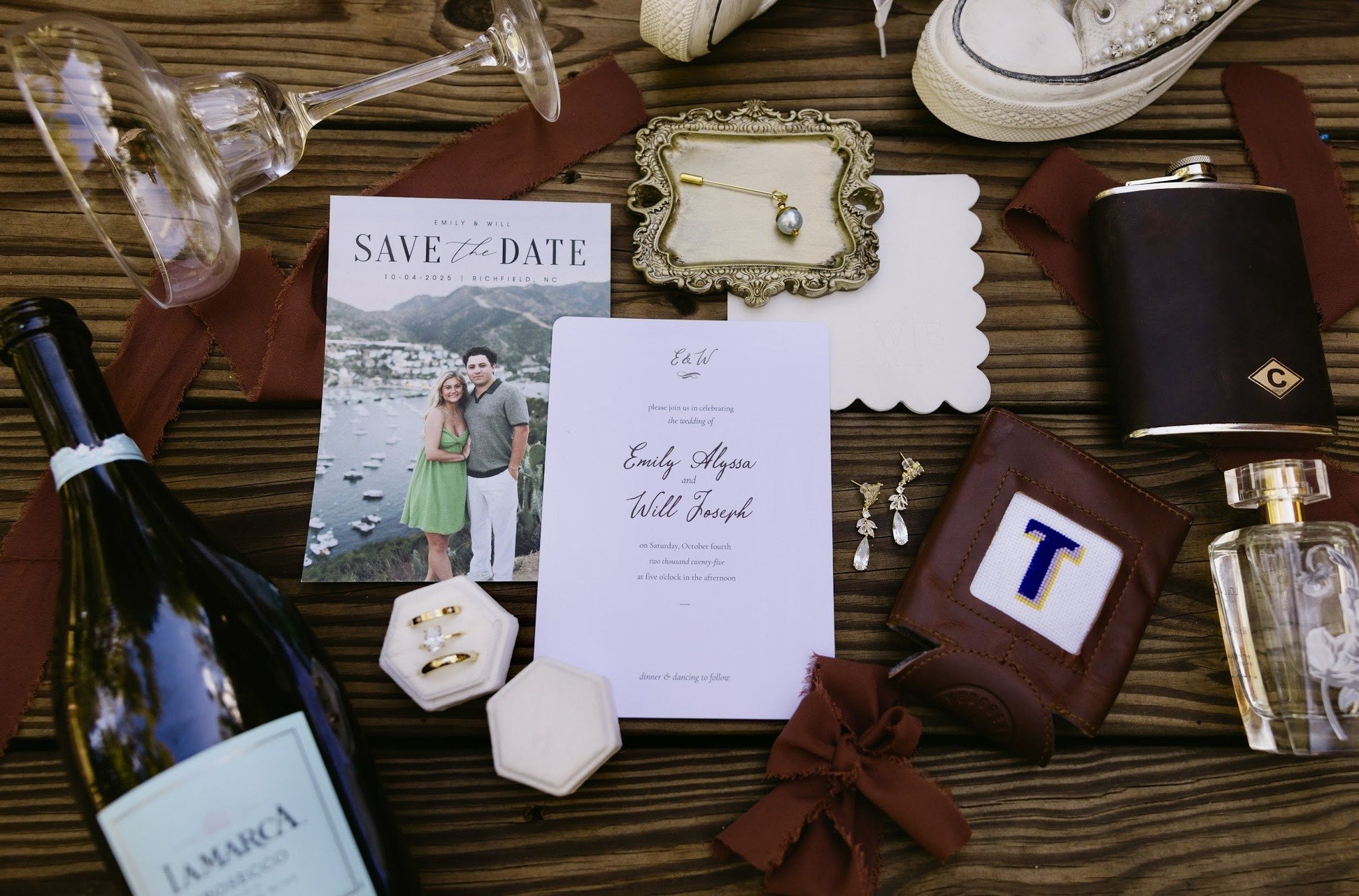 Wedding invitation with photos, jewelry, a perfume bottle, wine, glasses, and accessories arranged on a wooden surface.