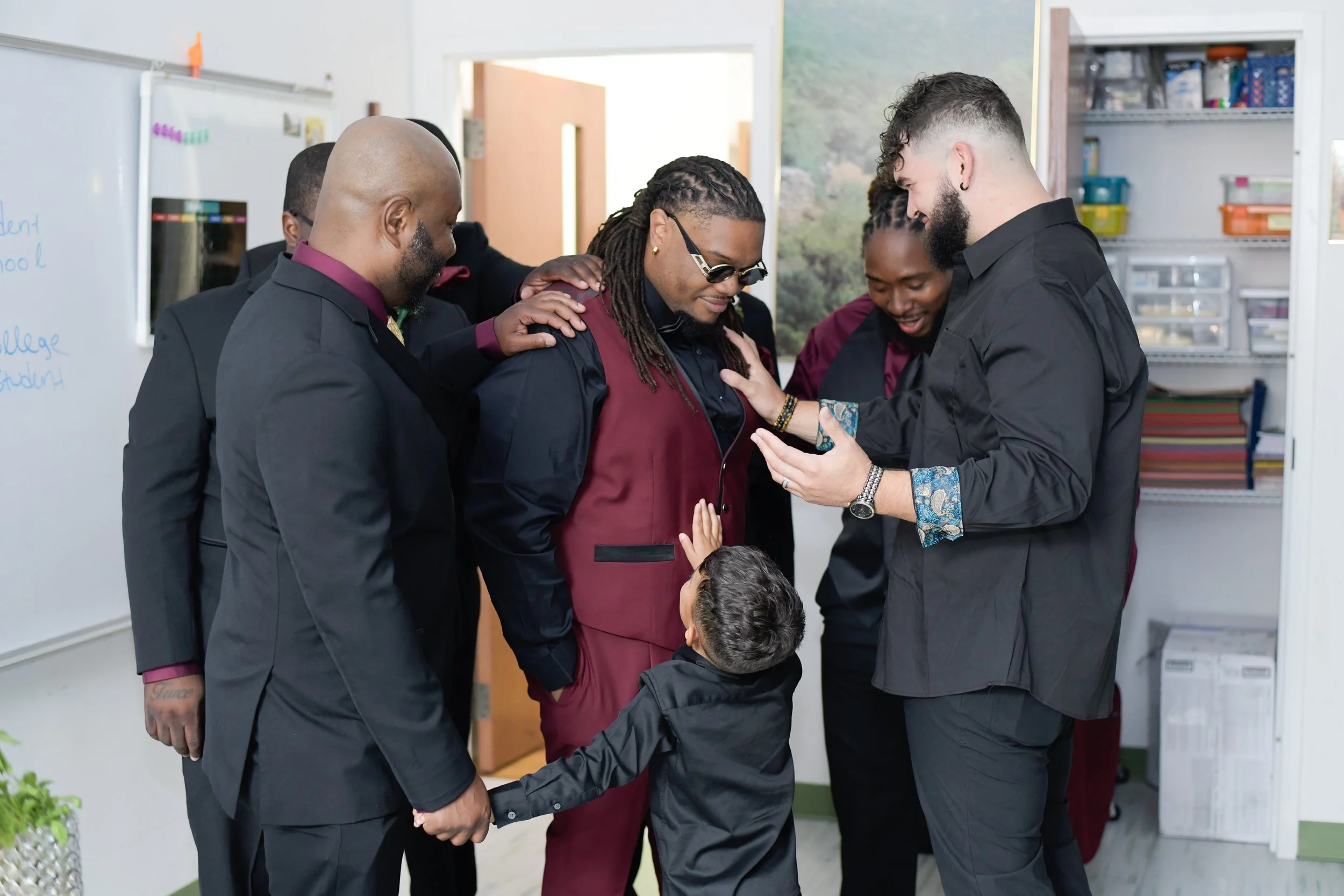 A group of six people, including a young boy, praying together in an office classroom setting.
