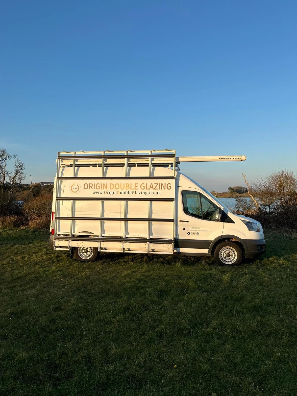 White Origin Double Glazing company van parked on grass with clear blue sky background.