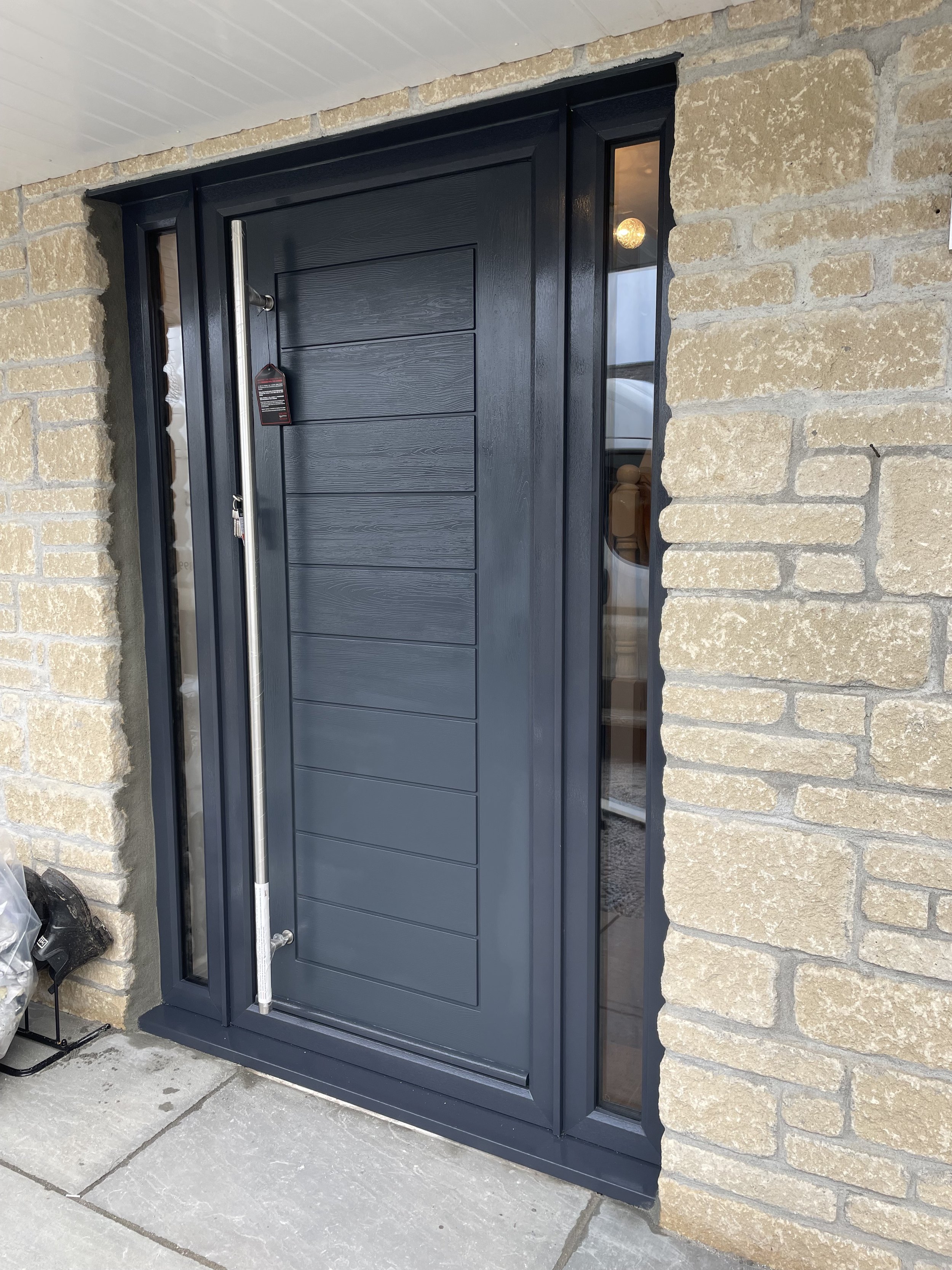 Modern blue front door with vertical handle, surrounded by stone brickwork, featuring side glass panels.