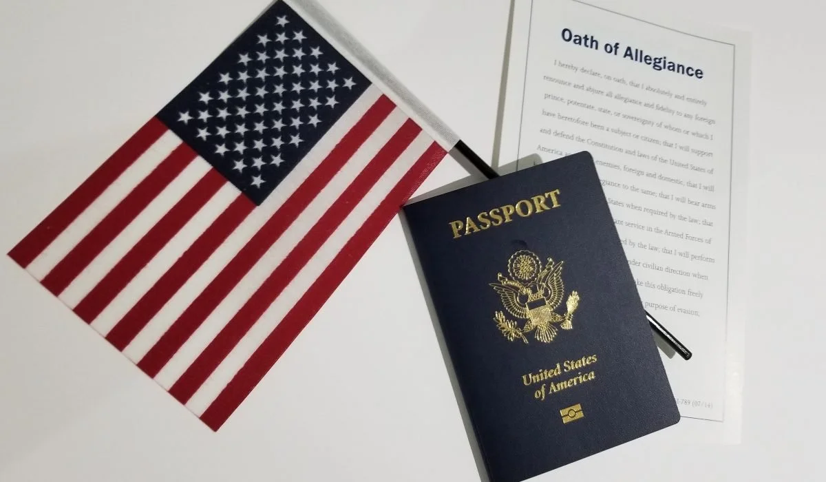 Una bandera de Estados Unidos, un pasaporte azul, y una hoja con la declaración de juramento de lealtad.