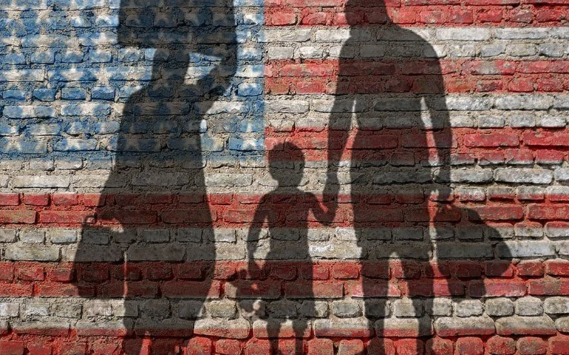 Sombras de una familia frente a una pared con bandera de Estados Unidos, con una mujer, un niño, un hombre y una niña
