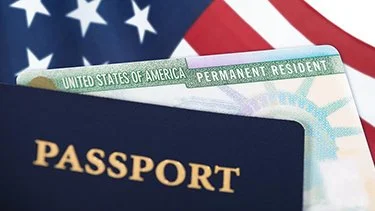 Un pasaporte y una tarjeta de residente permanente sobre una bandera de Estados Unidos.