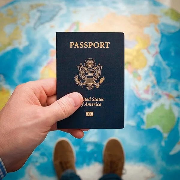 Persona sosteniendo un pasaporte de Estados Unidos con un mapa del mundo en el suelo.