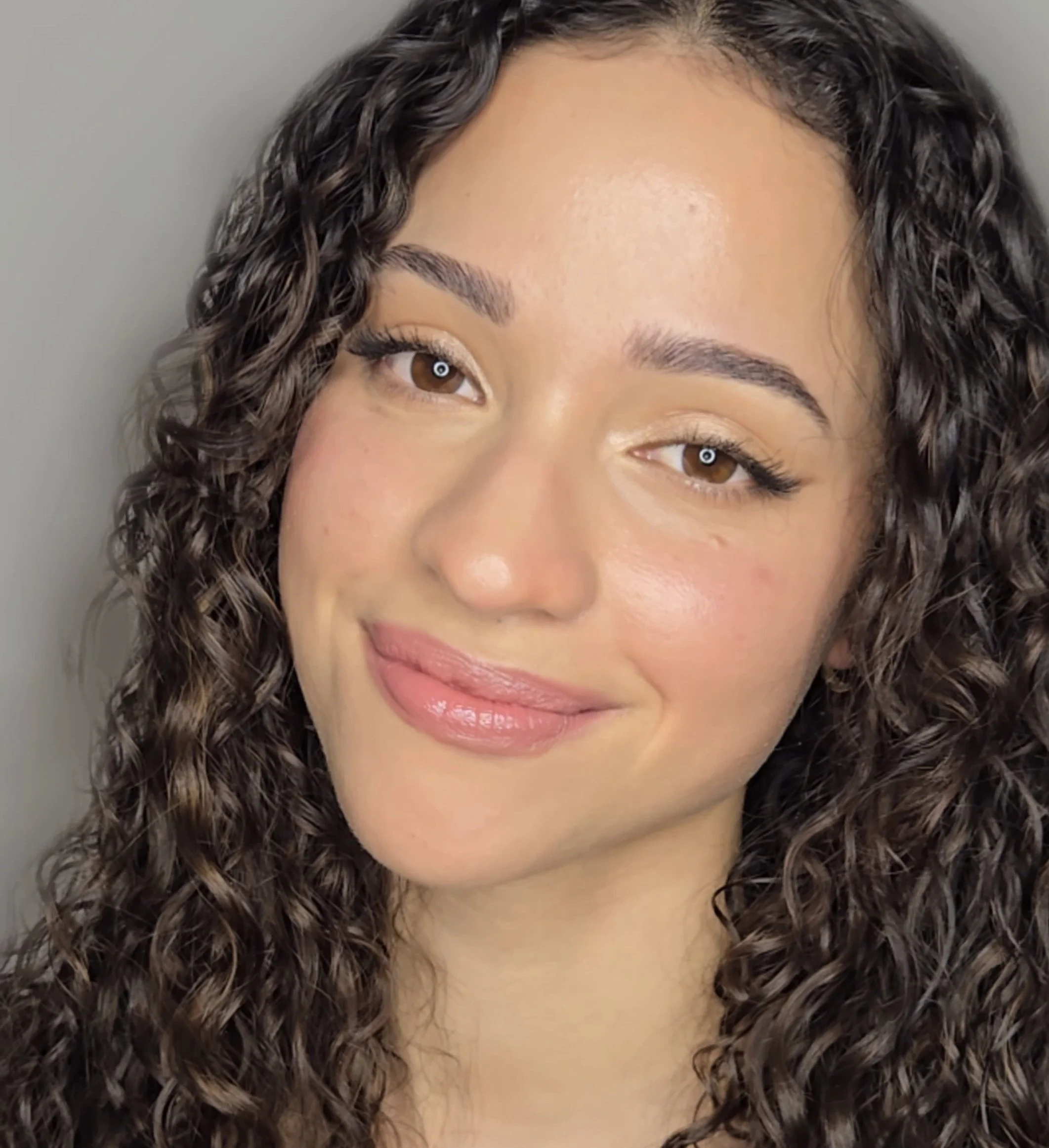 A luminous, signature beauty look showcasing a refined “lit-from-within” glow, groomed brows, and a natural glossy lip.